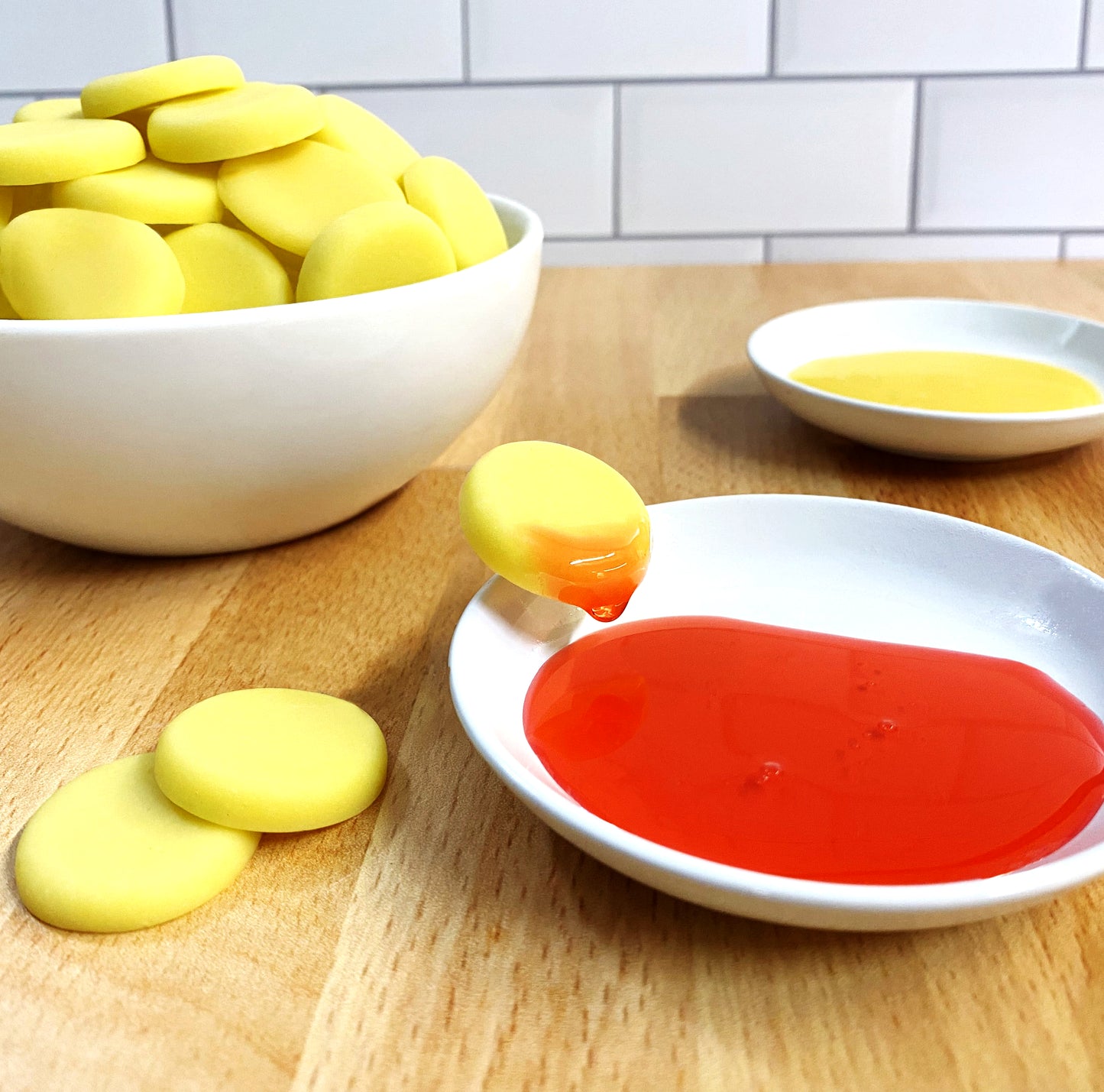 white bowl of gummy nachos and two white bowls of one red and one yellow dipping sauce with one gummy nacho dipped in the red sauce