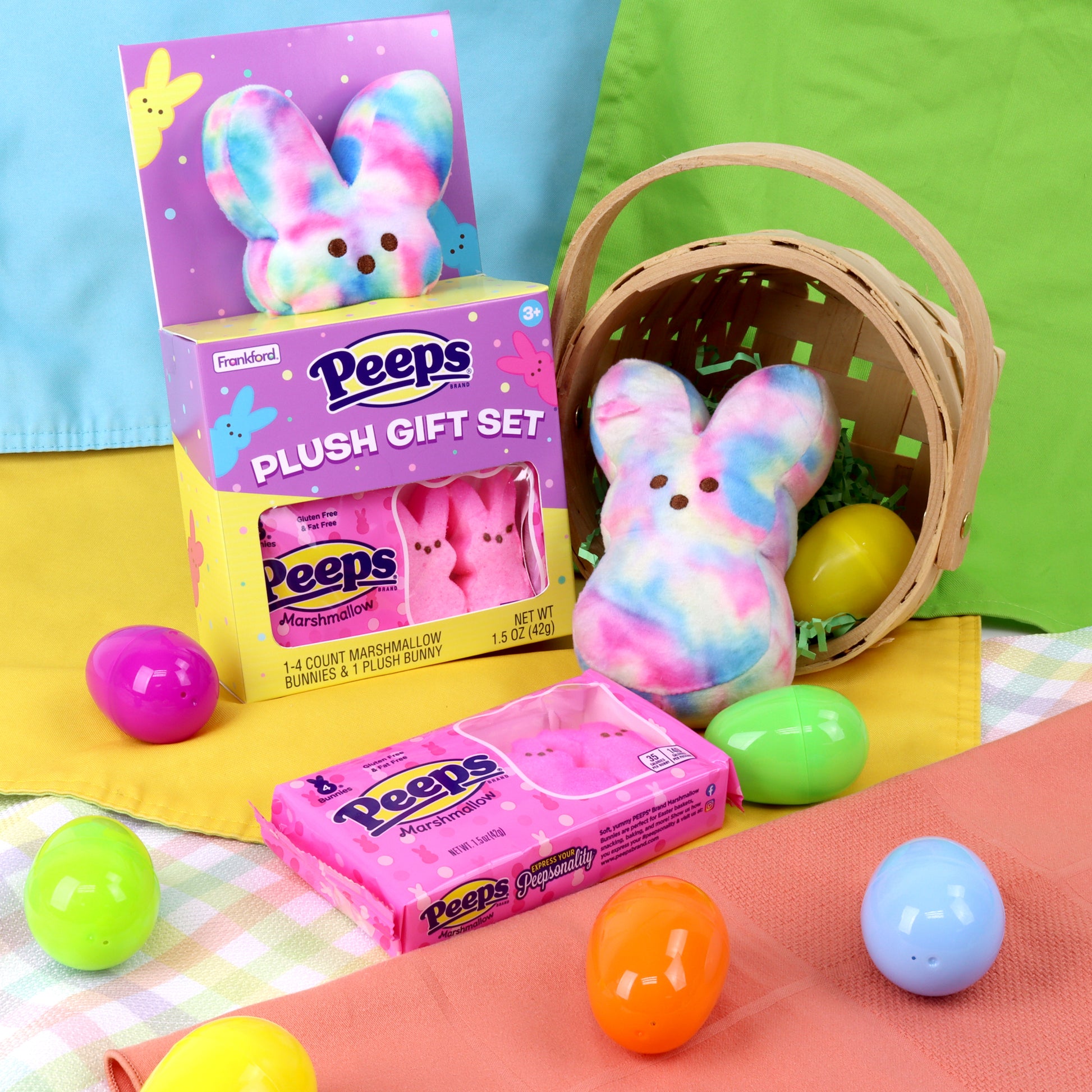 purple and yellow box with a tie dye plush bunny and pink peeps marshmallows and tie dye bunny and pink peeps in a basket with plastic eggs around