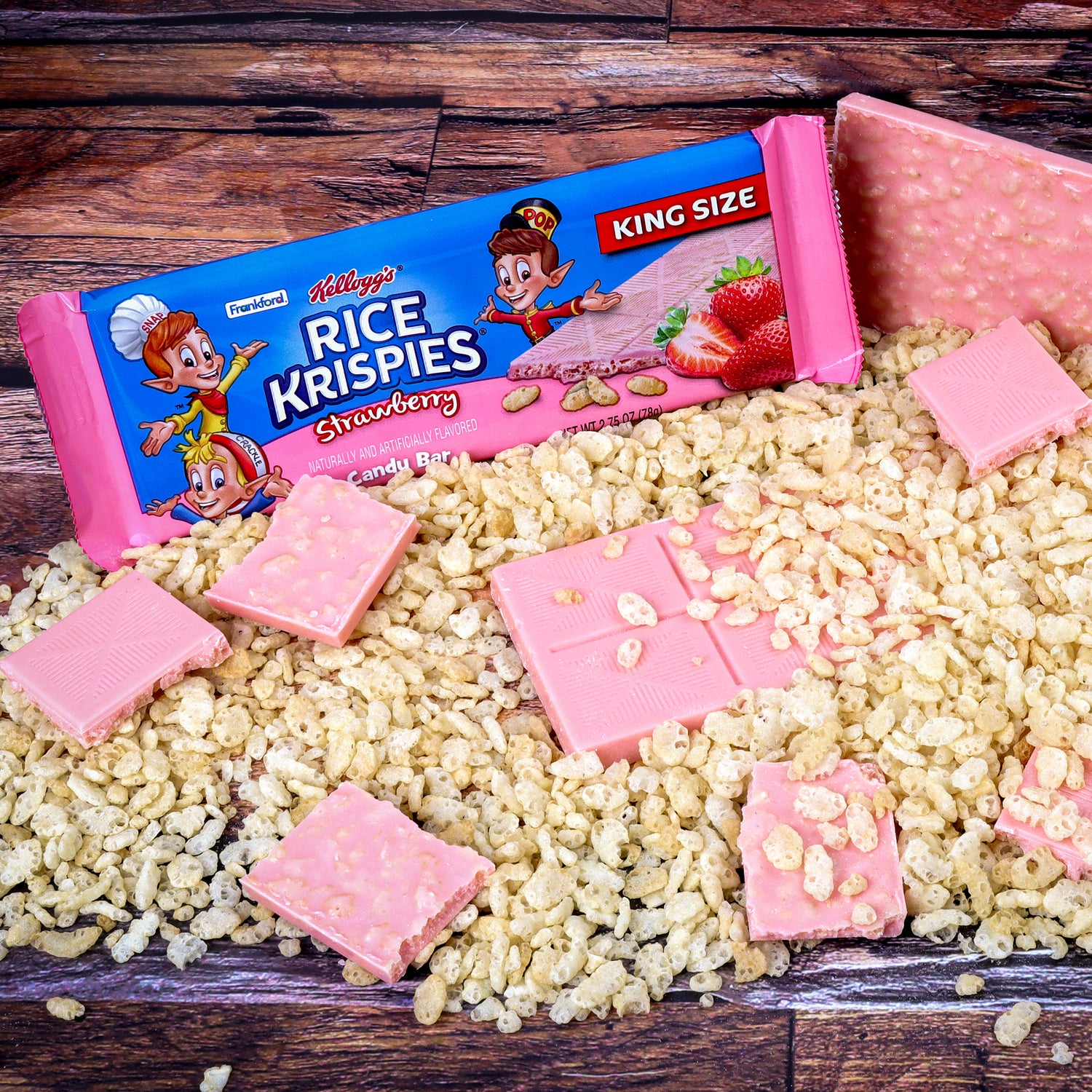 strawberry flavored rice krispies candy bar package and pieces over crisp rice cereal on a wooden background