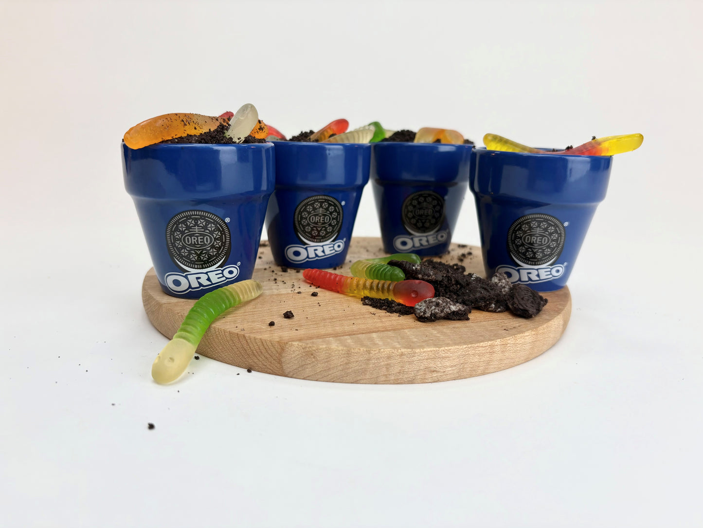 Four blue Oreo cookie buckets with snacks on a wooden board against a white background
