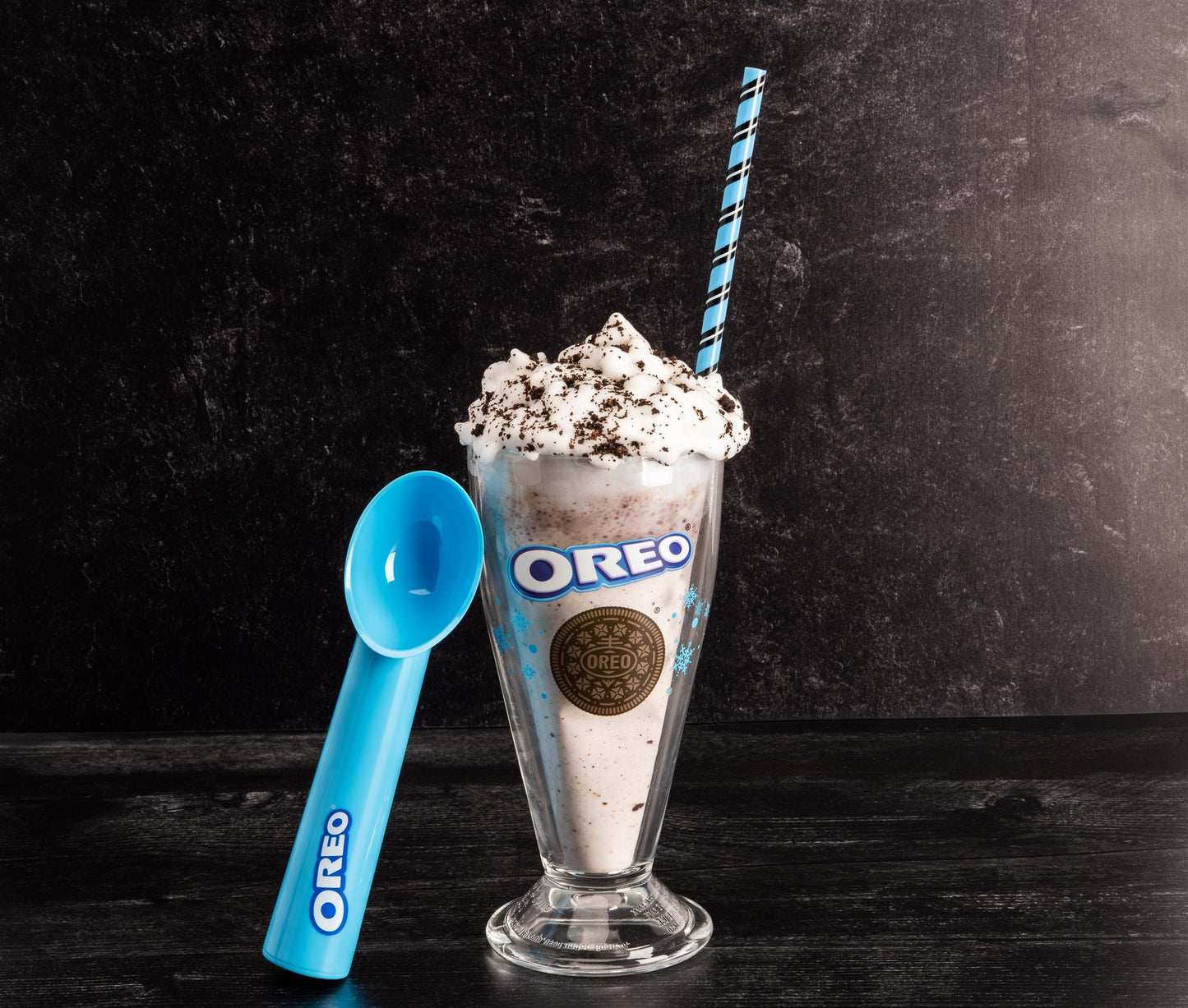 OREO milkshake with a blue straw and scoop on a dark background