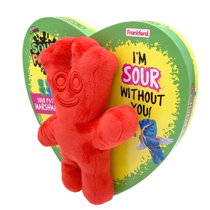 yellow heart shaped box with a green border and a red sour patch plush toy on the front