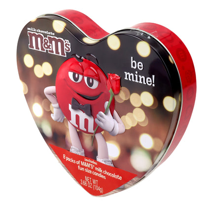 top angled view of a heart shaped tin with yellow circles in the background with a red M&M character holding a rose and the words be mine