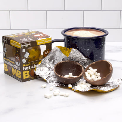 opened hot chocolate bomb with mini marshmallows, brown hot chocolate bomb box, and blue mug with hot chocolate