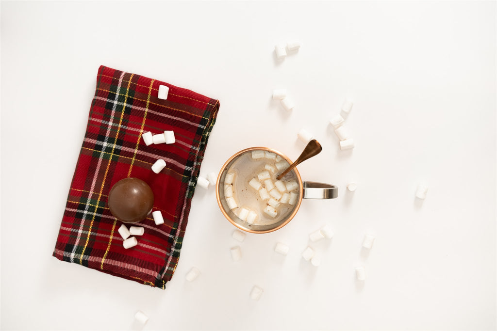 Hot chocolate bomb with marshmallows around it and a cupe of hot chocolate with marshmallows in it 