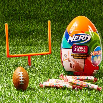 Orange plastic egg in grass with orange toy goal post, toy mini football, and smarties candies