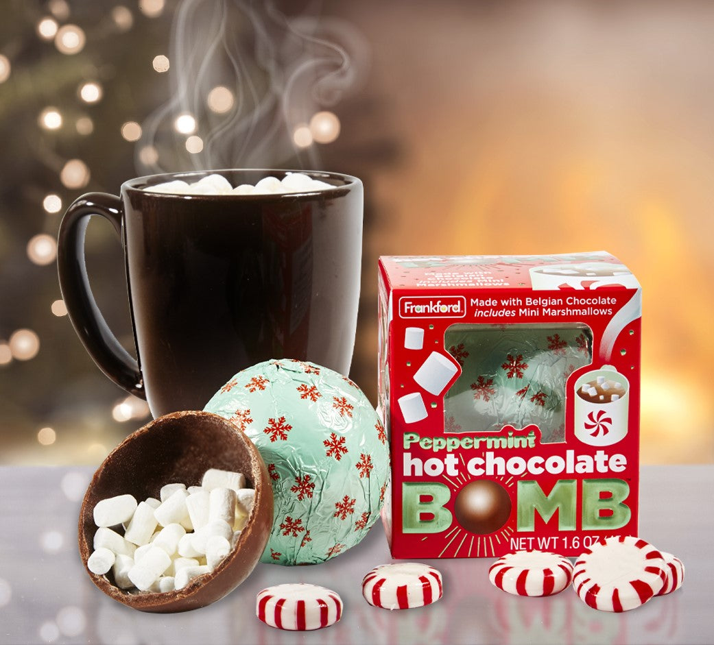 red christmas themed hot chocolate bomb box, brown mug with hot chocolate and mini marshmallows, opened hot chocolate bomb with mini marshmallows, green foil wrapped with red snowflakes hot chocolate bomb, and peppermints
