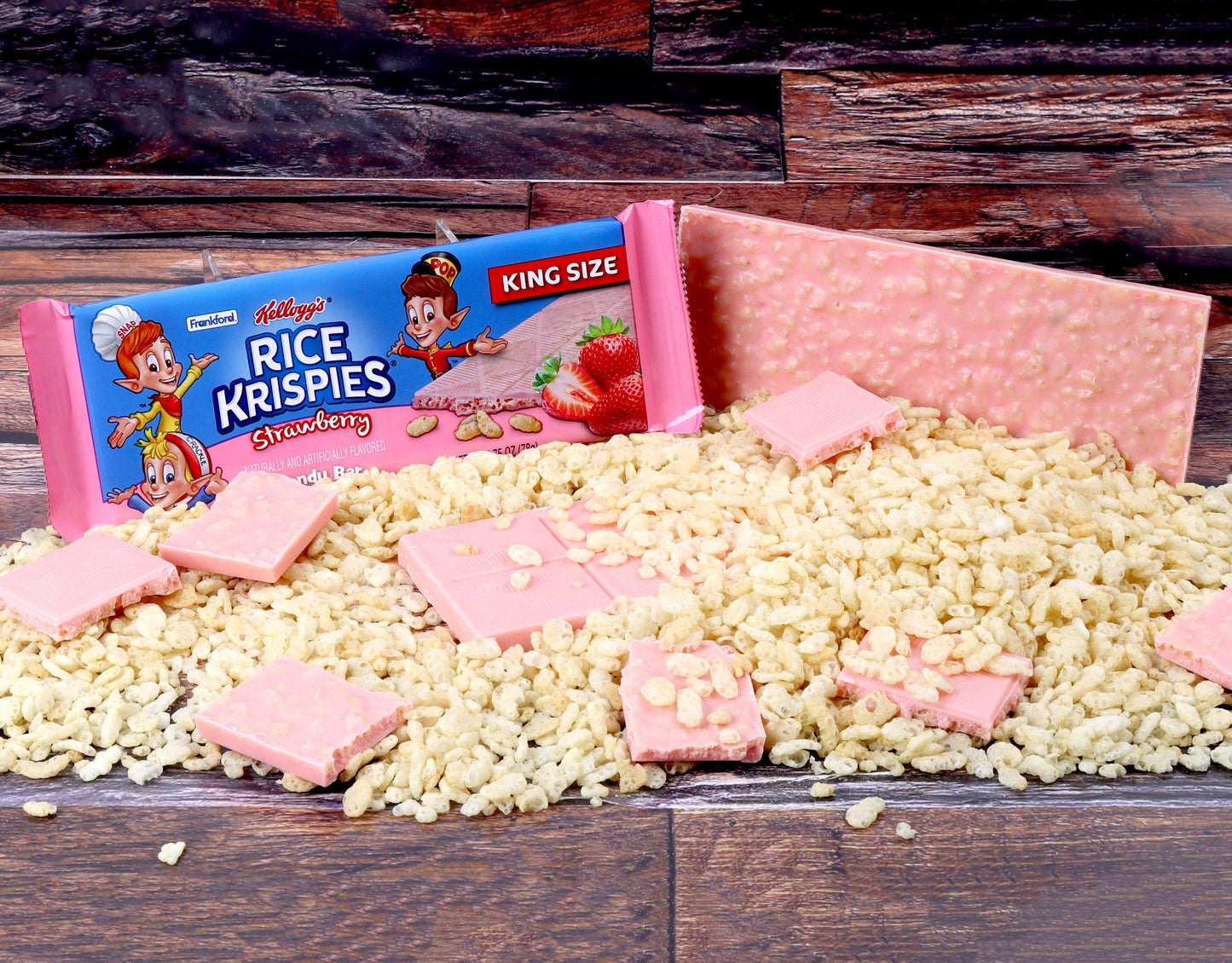 Blue and pink candy bar wrapper surrounded by broken pieces of pink candy bar and rice krispies cereal