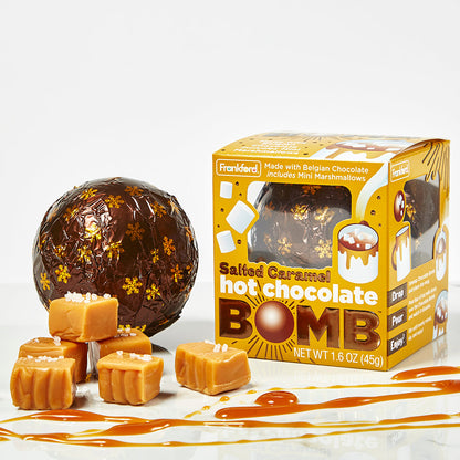 yellow hot chocolate bomb box next to brown and snowflake print foil wrapped hot chocolate bomb with pieces of salted caramel