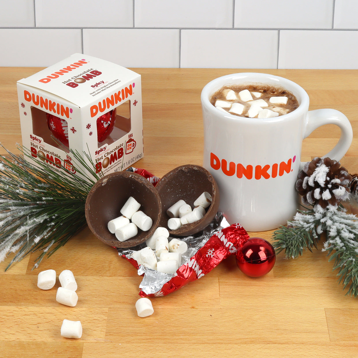 white christmas themed box with red foil with Dunkin' logo wrapped hot chocolate bomb, white Dunkin' mug with hot chocolate and mini marshmallows, and broken hot chocolate bomb with mini marshmallows
