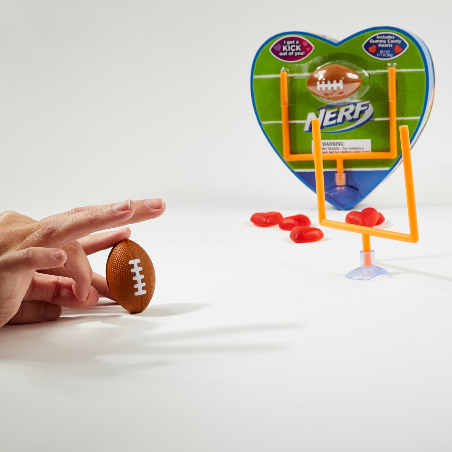 heart shaped box with red heart shaped gummies and hand playing with toy brown football and toy orange goal post