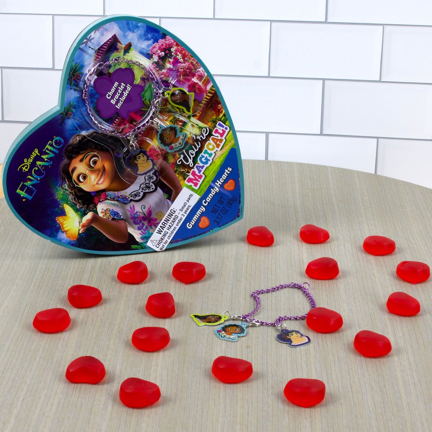 Blue Heart shaped box on its side surrounded by red heart shaped gummy candies and purple character charm bracelet