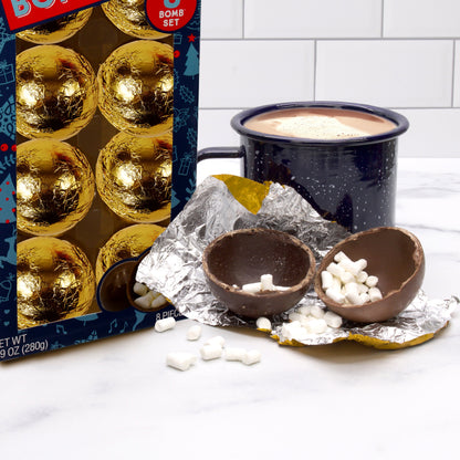 Navy themed Christmas box with 8 gold foil wrapped hot chocolate bombs, a cup of hot chocolate, and a broken hot chocolate bomb with mini martshmallows